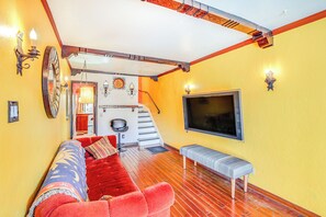 A living room with a red sofa, a bench, a TV mounted on the wall, and a staircase leading to another room. - 1 Mi to Ocean! Home w/ Rooftop Deck in Long Beach (Long Beach)