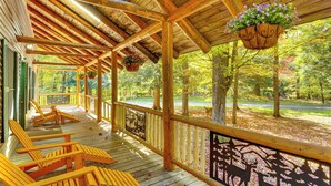 Un portico coperto con ringhiere in legno, un cesto di fiori appeso e diverse sedie di legno.