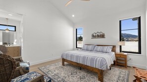 A bedroom with a bed, a nightstand, a chair, a dresser, a mirror, and a window with a view of mountains. - Beartooth View (Red Lodge)