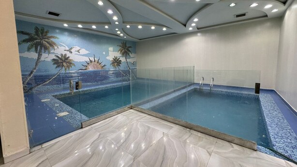 Una piscina con un mural tropical, paredes de vidrio transparente y piso de baldosas.