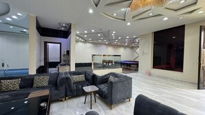 Una habitación amplia con mesa de billar, billares y una zona de estar con sofás y una mesita.