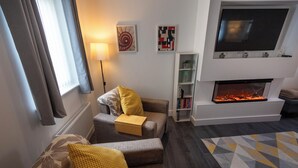 Een moderne woonkamer met een bank, een open haard, een televisie en een boekenkast.