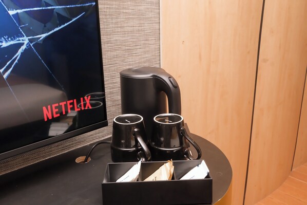 A TV displaying 'NETFLIX' with a coffee maker and two mugs on a table.