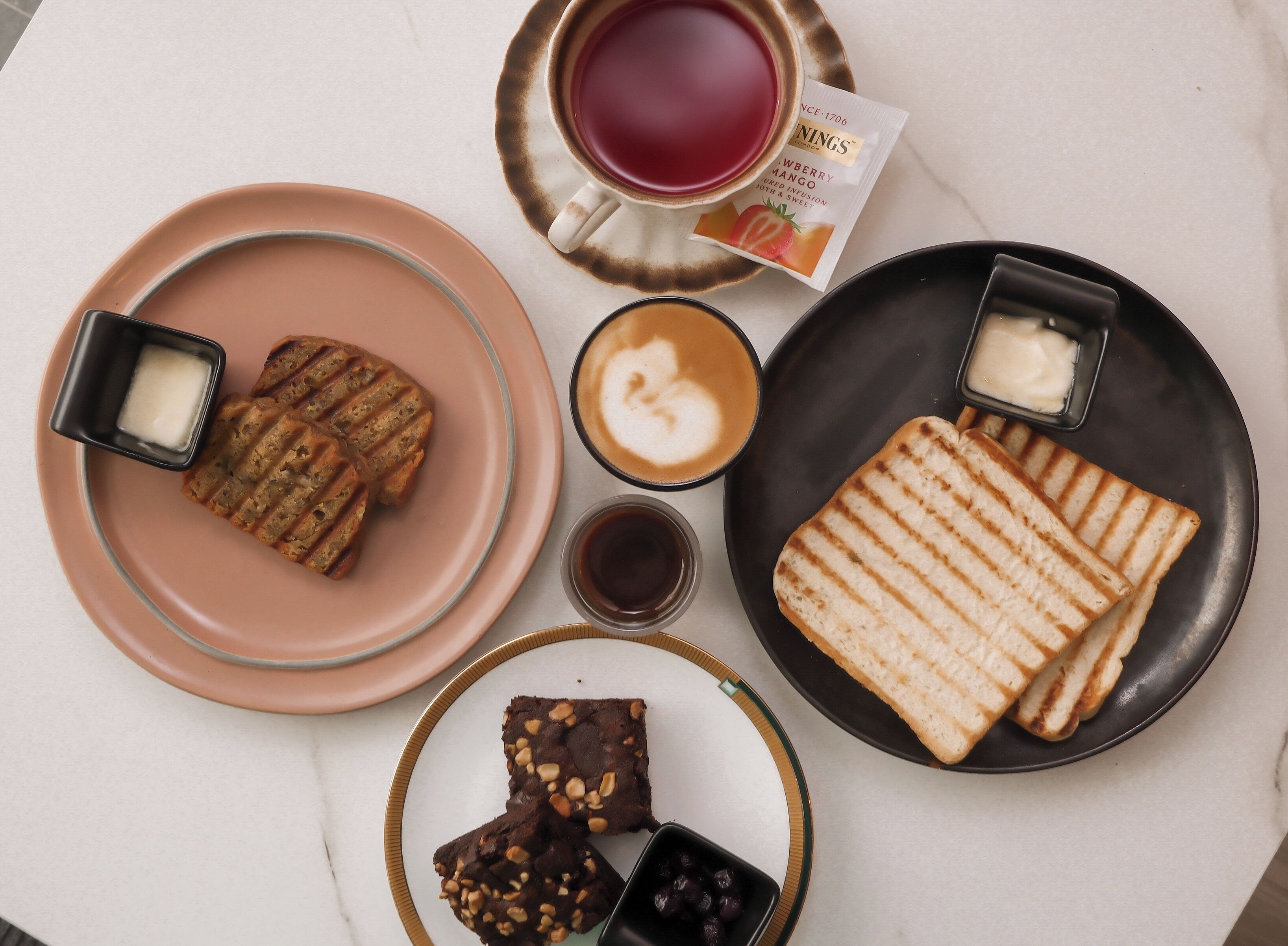 Ett bord med olika sorters mat, inklusive våfflor, en muffin, brownies och en kopp te.
