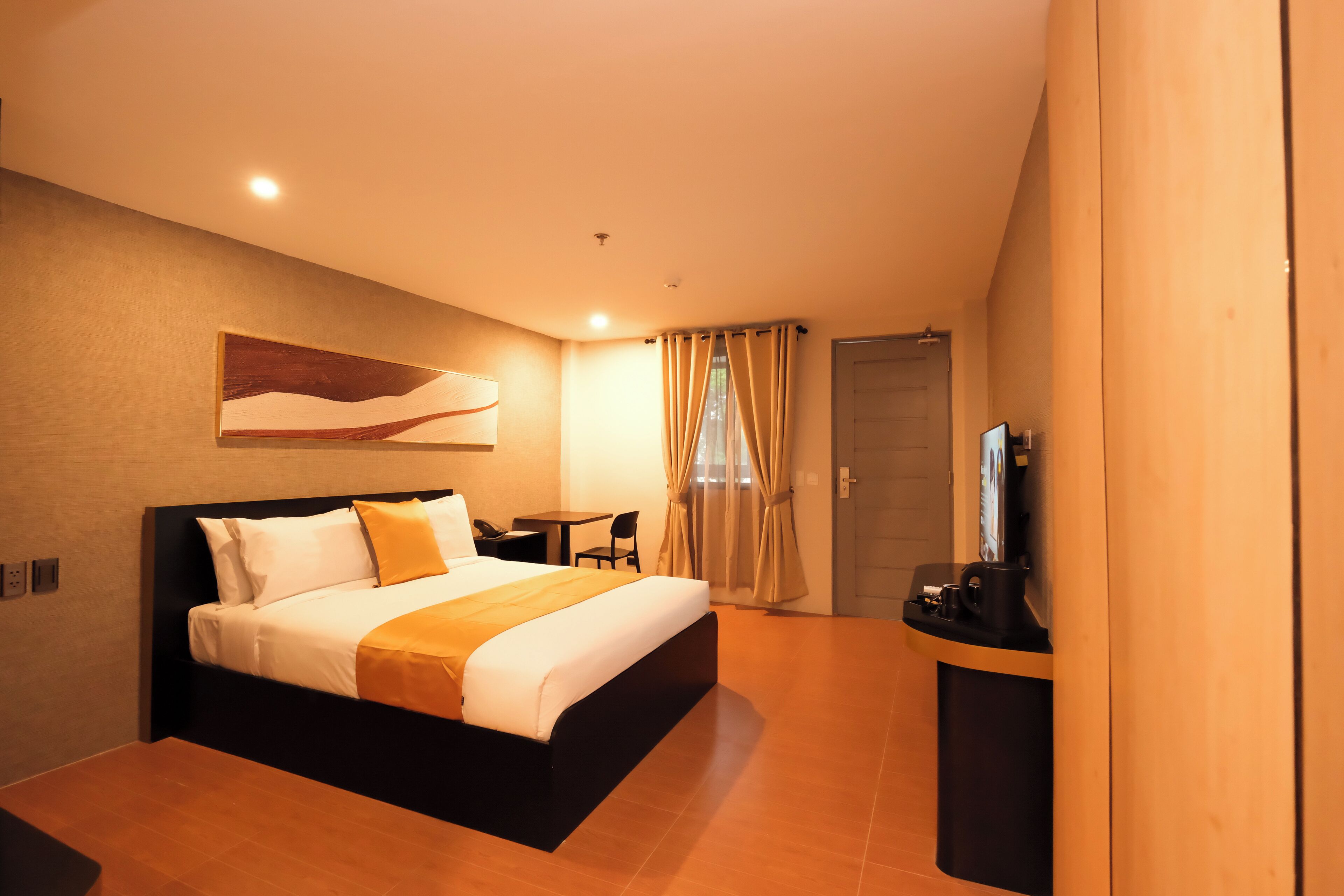 A hotel room with a large bed, a desk with a chair, a TV, and a door.