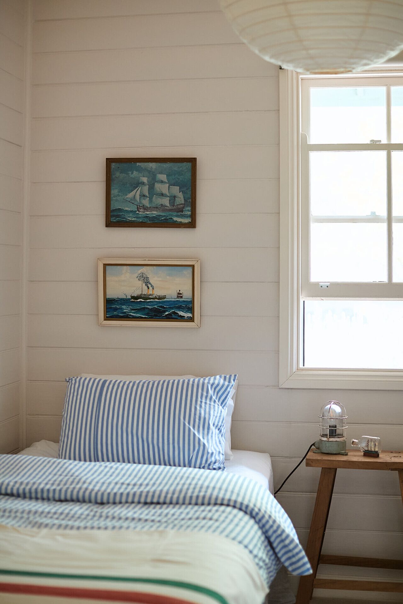 Une chambre à coucher avec un lit, deux tableaux encadrés, une fenêtre et une petite table avec une lampe.