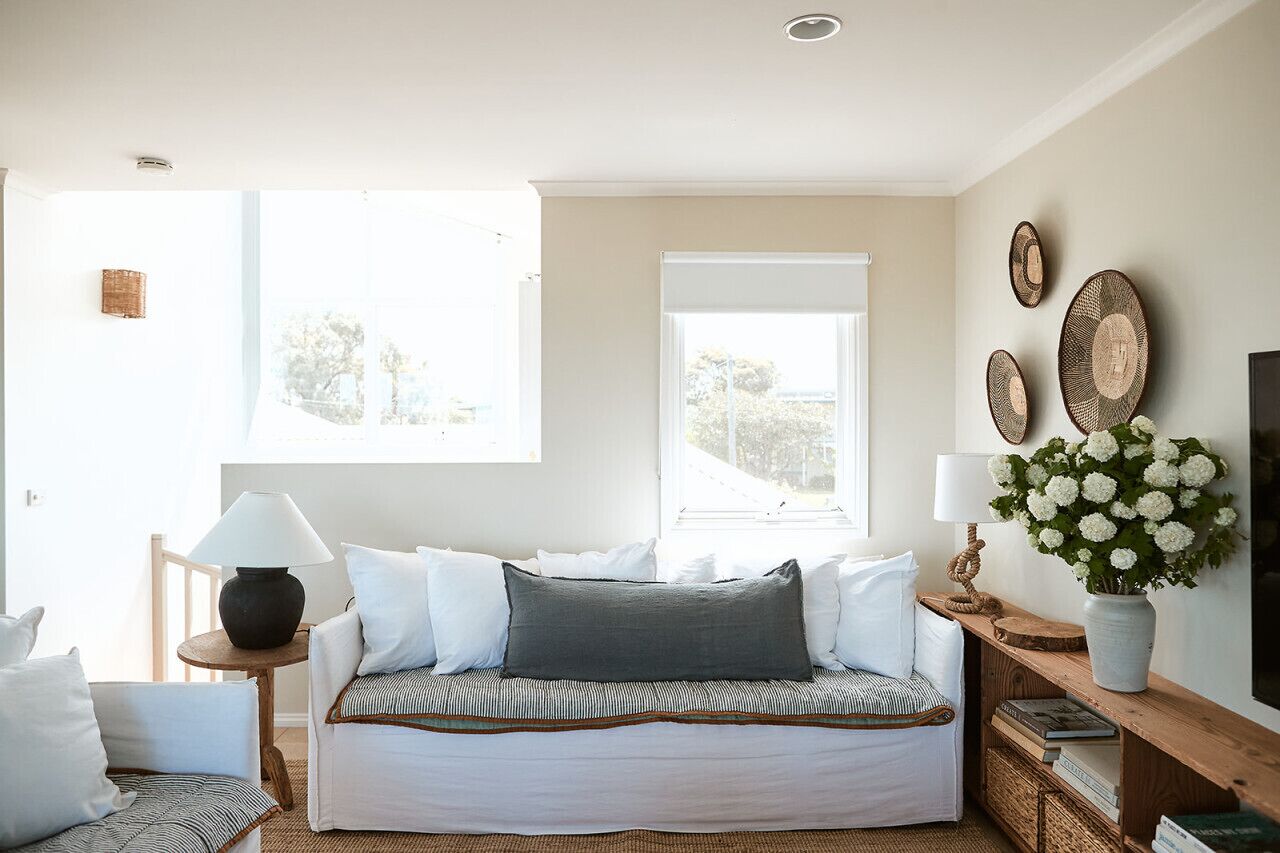 Un salon chaleureux avec un canapé, une table d’appoint avec une lampe, un banc en bois et une grande fenêtre laissant entrer la lumière naturelle.