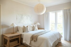 Un dormitorio con una cama grande, dos lámparas de noche, una lámpara colgante, una ventana con cortinas y una obra de arte en la pared.