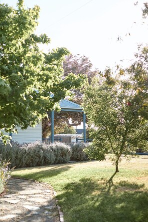 Um gazebo com telhado azul, cercado por arbustos bem cuidados e gramado.