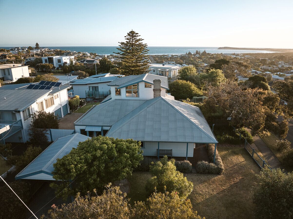 A residential area with houses featuring modern architecture, solar panels, and a coastal view.