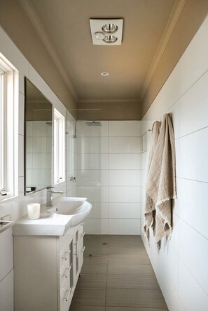 Un baño moderno con un espejo grande, dos lavamanos, un perchero para toallas y una zona de ducha.