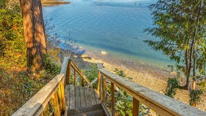 Eine Holztreppe führt zu einem Strand mit klarem Wasser und Blick auf die Küste.
