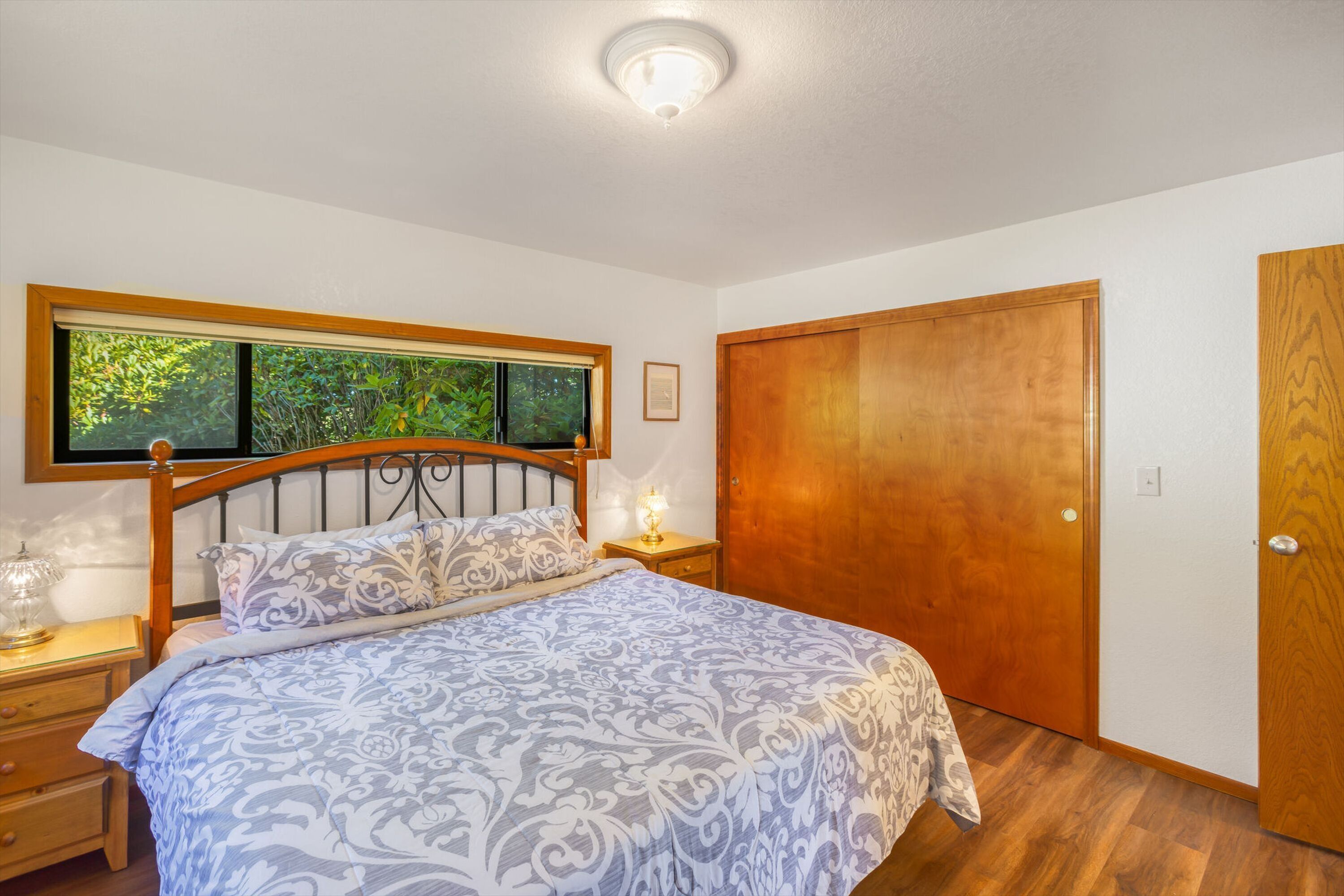 A bedroom with a bed, wooden headboard, bedside tables, a nightstand, a wooden door, and a framed picture on the wall.