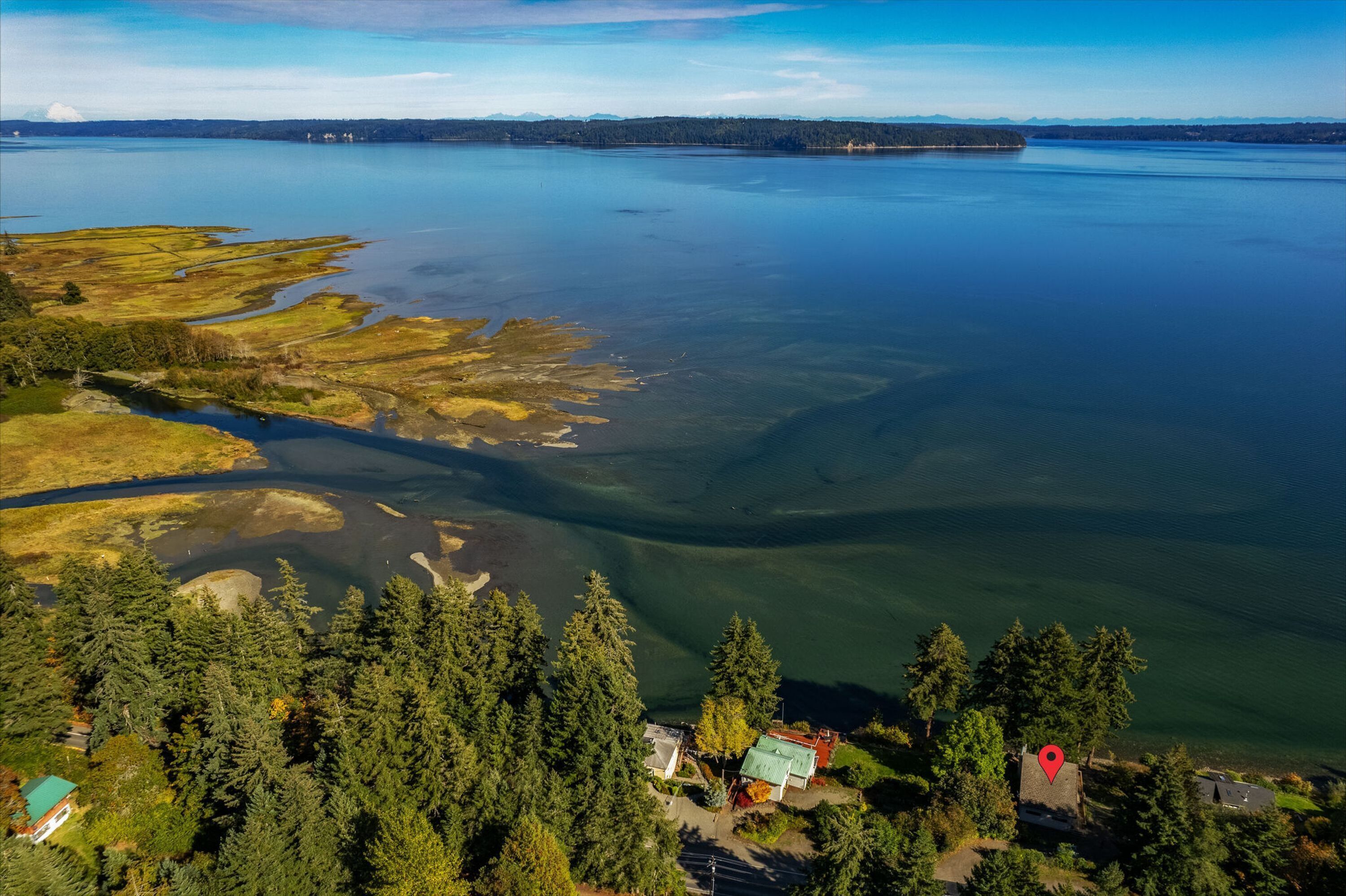 Vue aérienne d’une propriété au bord d’un lac, avec une eau claire, entourée d’une forêt dense, et comprenant plusieurs bâtiments dont les toits et les structures sont bien visibles.