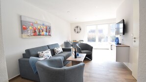 A modern living room with a grey sofa, two armchairs, a coffee table, and a painting on the wall. - Vacation apartment Molle (Norden)