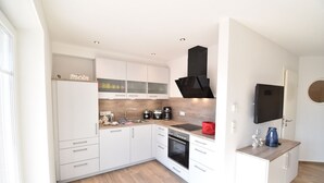A modern kitchen with white cabinetry, a black range hood, and a wooden countertop. - Vacation apartment Molle (Norden)