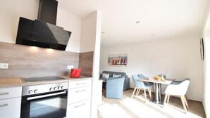 A modern kitchen with a built-in oven, a dining area with blue chairs, and a painting on the wall. - Vacation apartment Molle (Norden)