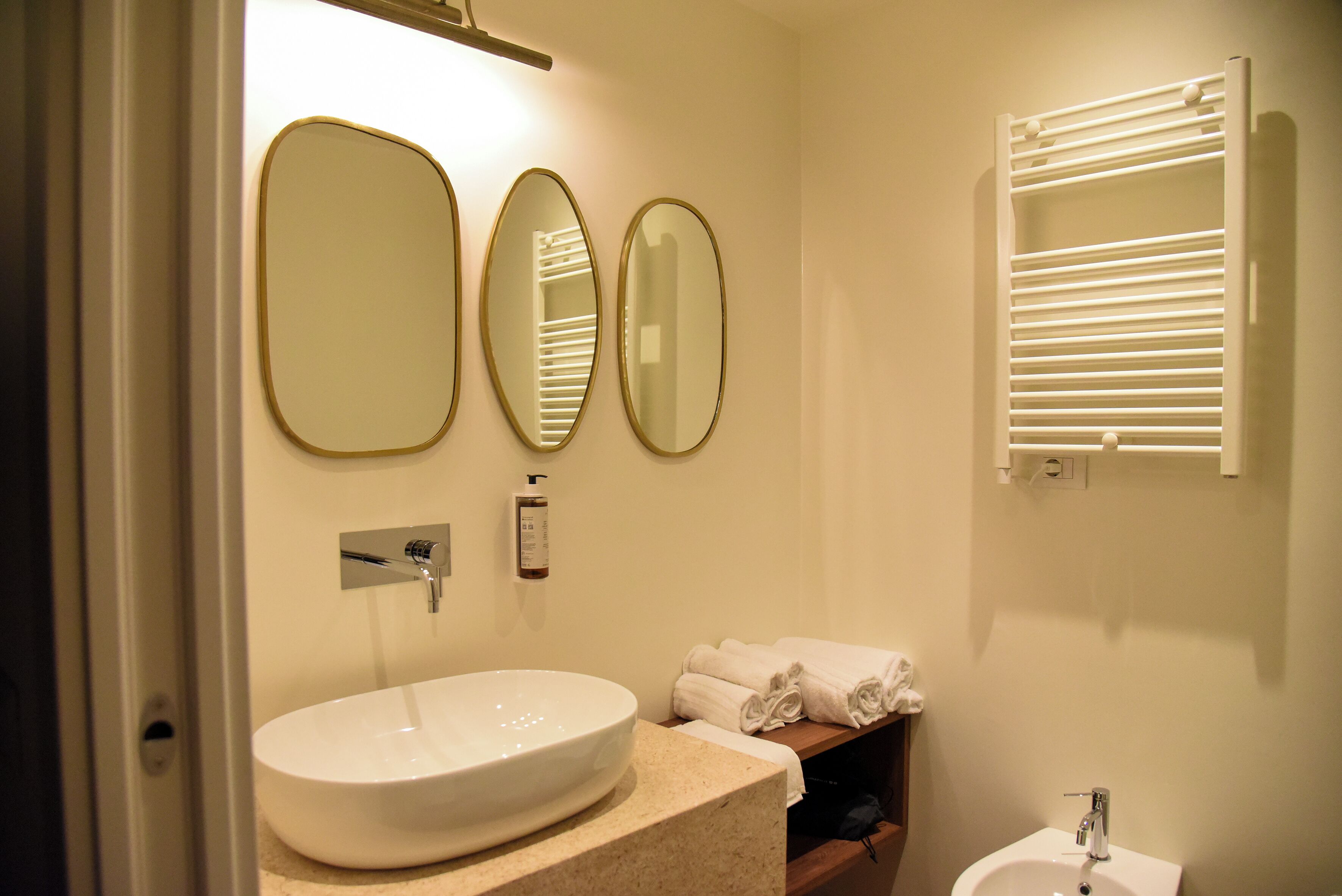 Un bagno con un ampio lavabo ovale, due specchi a parete, un portascope con asciugamani piegati e un piccolo lavandino su piedistallo.