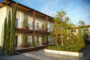 Un immeuble moderne à plusieurs étages, doté de balcons, d’un espace extérieur aménagé pour s’asseoir et d’un jardin paysager.