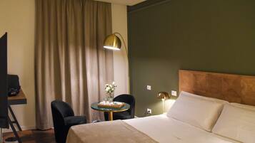 A hotel room with a bed, a desk, a chair, a table with a vase of flowers, and a lamp.