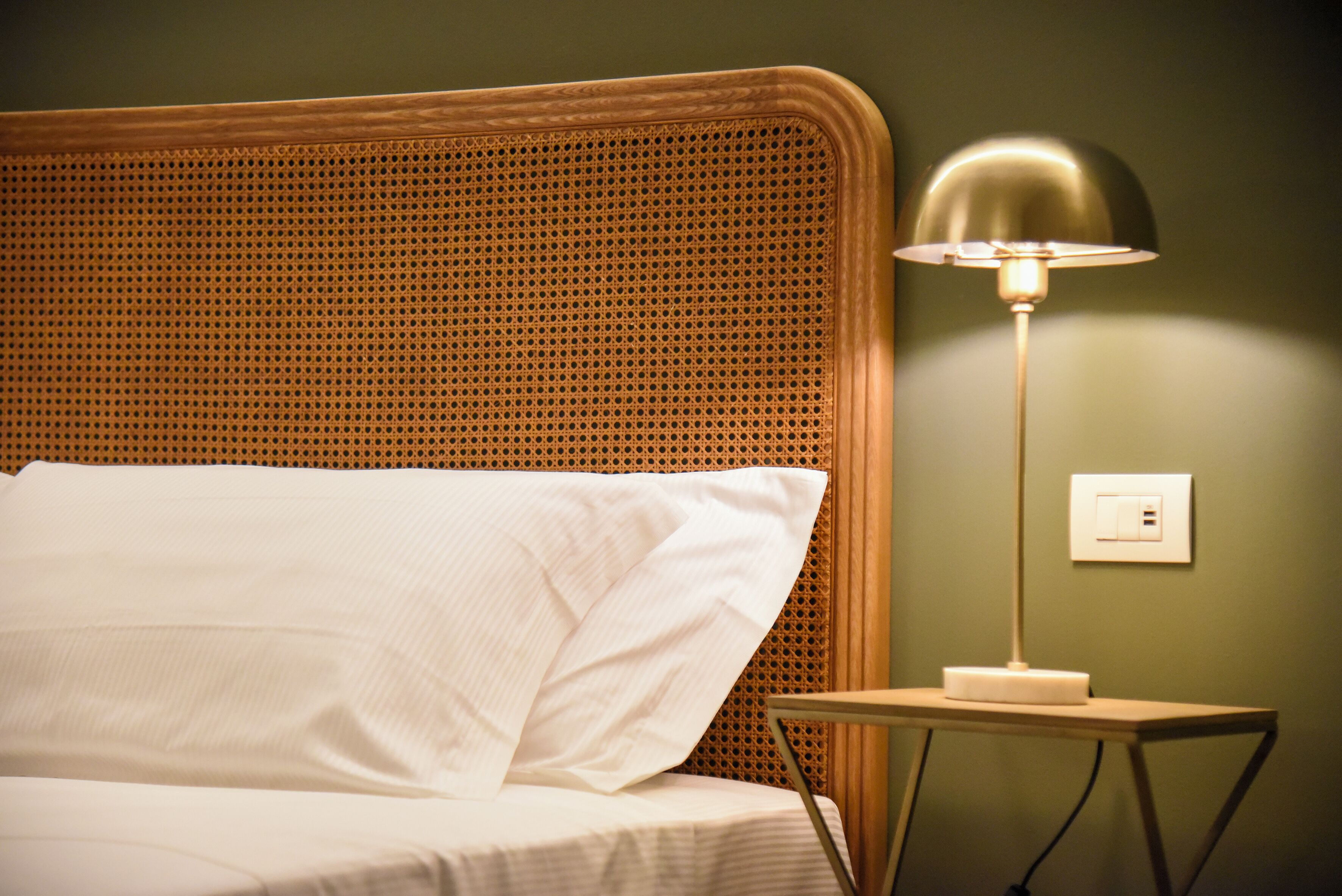 A bed with white linens, a wooden headboard, and a bedside table with a lamp.