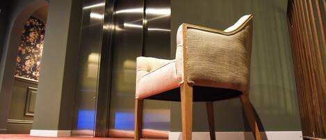 A chair in a room with a carpeted floor, a wall with a floral pattern, and a metallic elevator door.