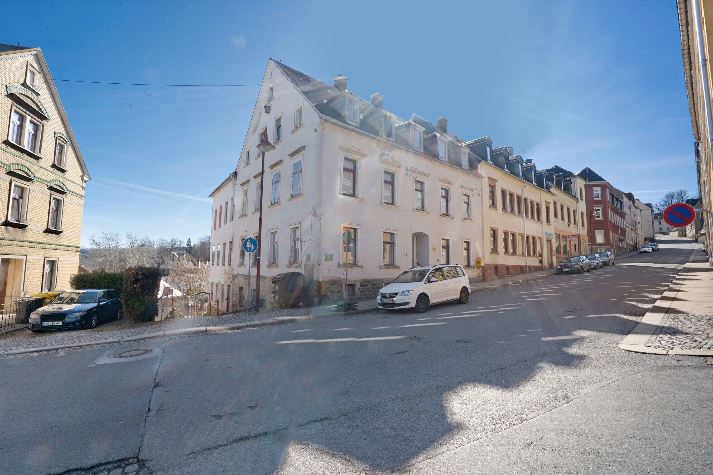 A street with buildings, a no parking sign, and a car parked on the side.