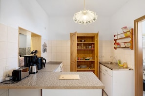 Une cuisine dotée de plans de travail en granit, d’un meuble en bois contenant de la vaisselle, d’une machine à café et d’un luminaire suspendu.
