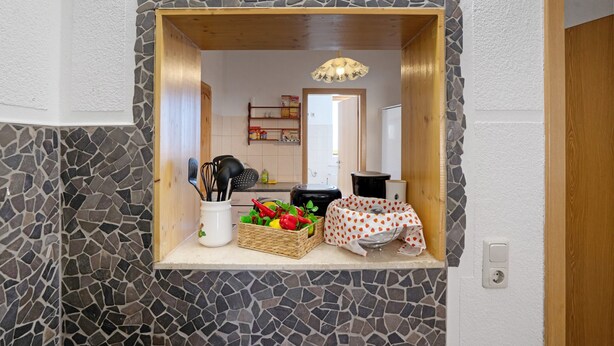 Une cuisine avec un pare-feu en pierre, un plan de travail en bois, un panier de produits frais et un luminaire suspendu.