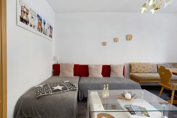A modern room with two beds, a sofa, a dining table, and a chandelier.