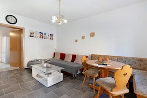 Un salon moderne comprenant un canapé, une table basse en verre, une table à manger en bois avec des chaises, une horloge au mur et un lustre.