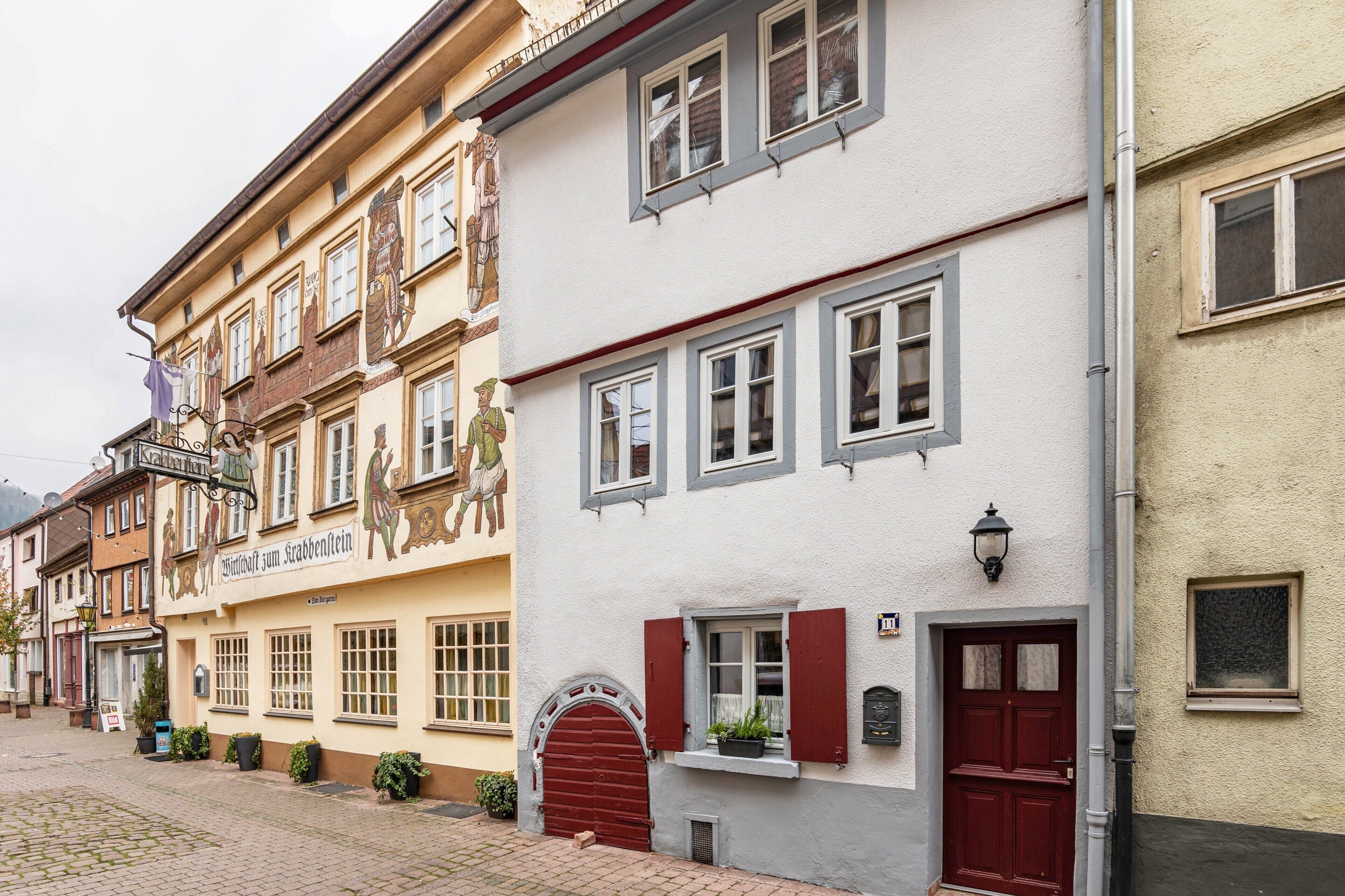 A row of traditional European buildings with distinct architectural styles, including a building with a red door and a sign indicating a restaurant.
