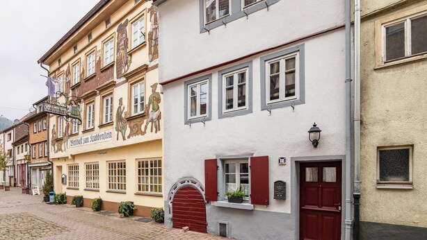 Une rangée de bâtiments européens traditionnels, chacun présentant un style architectural distinct, dont un bâtiment avec une porte rouge et une enseigne indiquant qu’il s’agit d’un restaurant.