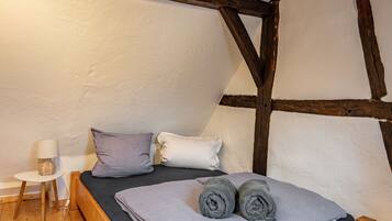 Ein Schlafzimmer mit einem hölzernen Bett, Kissen, einem kleinen Nachttisch mit Lampe und einer Wand mit freiliegenden Balken.
