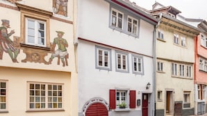Una hilera de edificios europeos tradicionales con características arquitectónicas destacadas, incluyendo una puerta roja y un pequeño balcón con una planta en maceta.