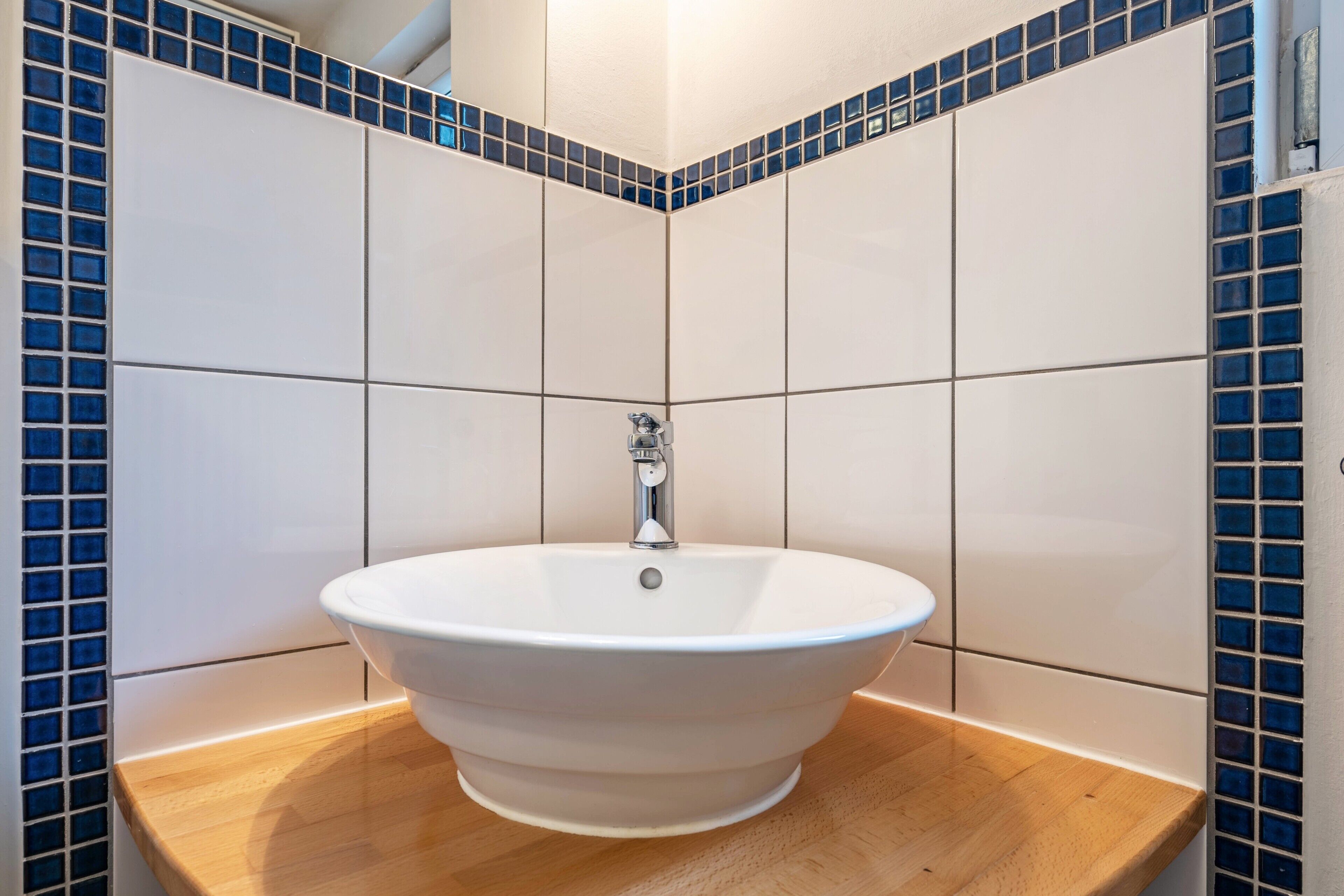 Un baño con un lavamanos blanco, mosaicos azules y una encimera de madera.
