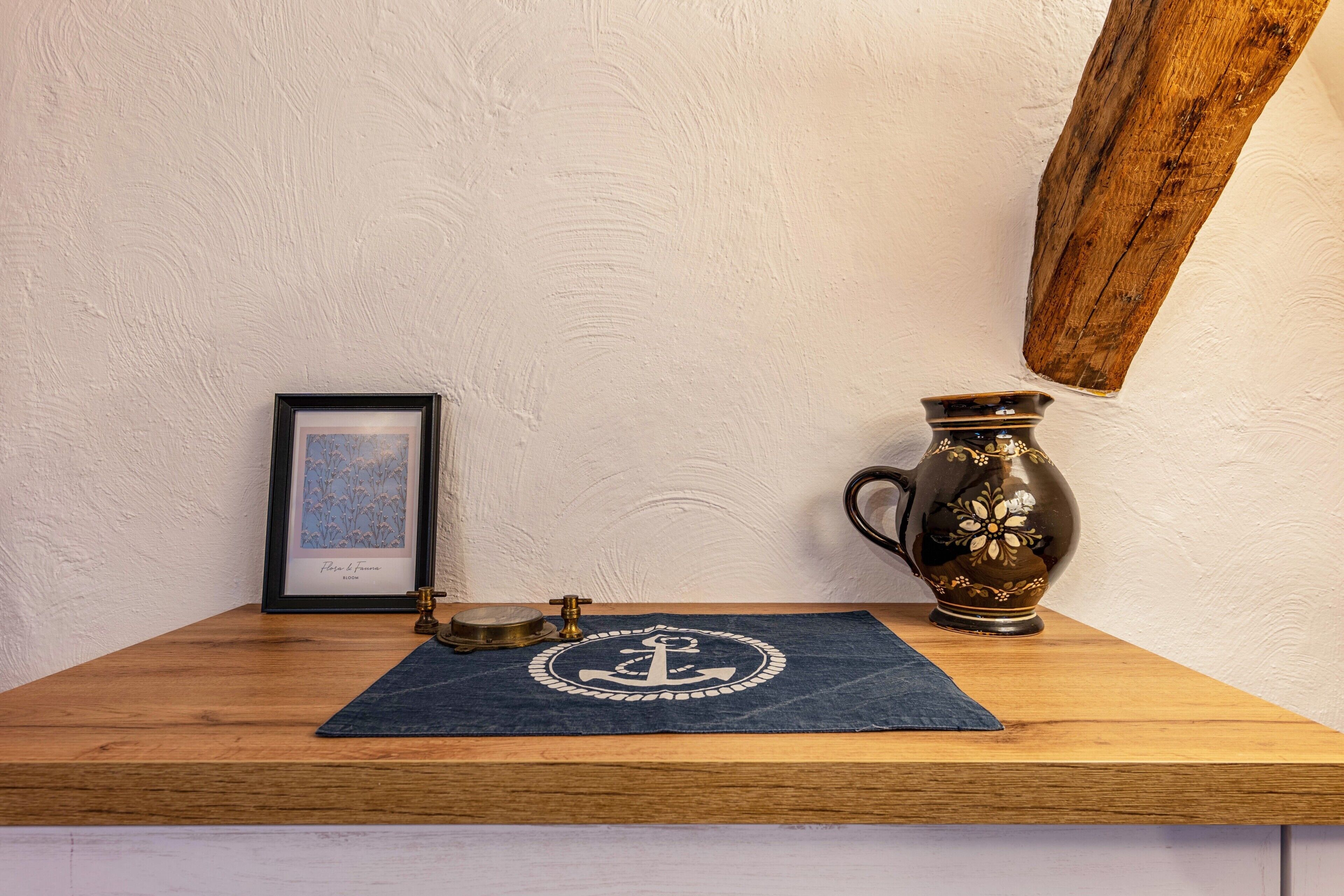 Une table en bois sur laquelle sont posés un tableau encadré, un objet en laiton et un pichet décoratif.