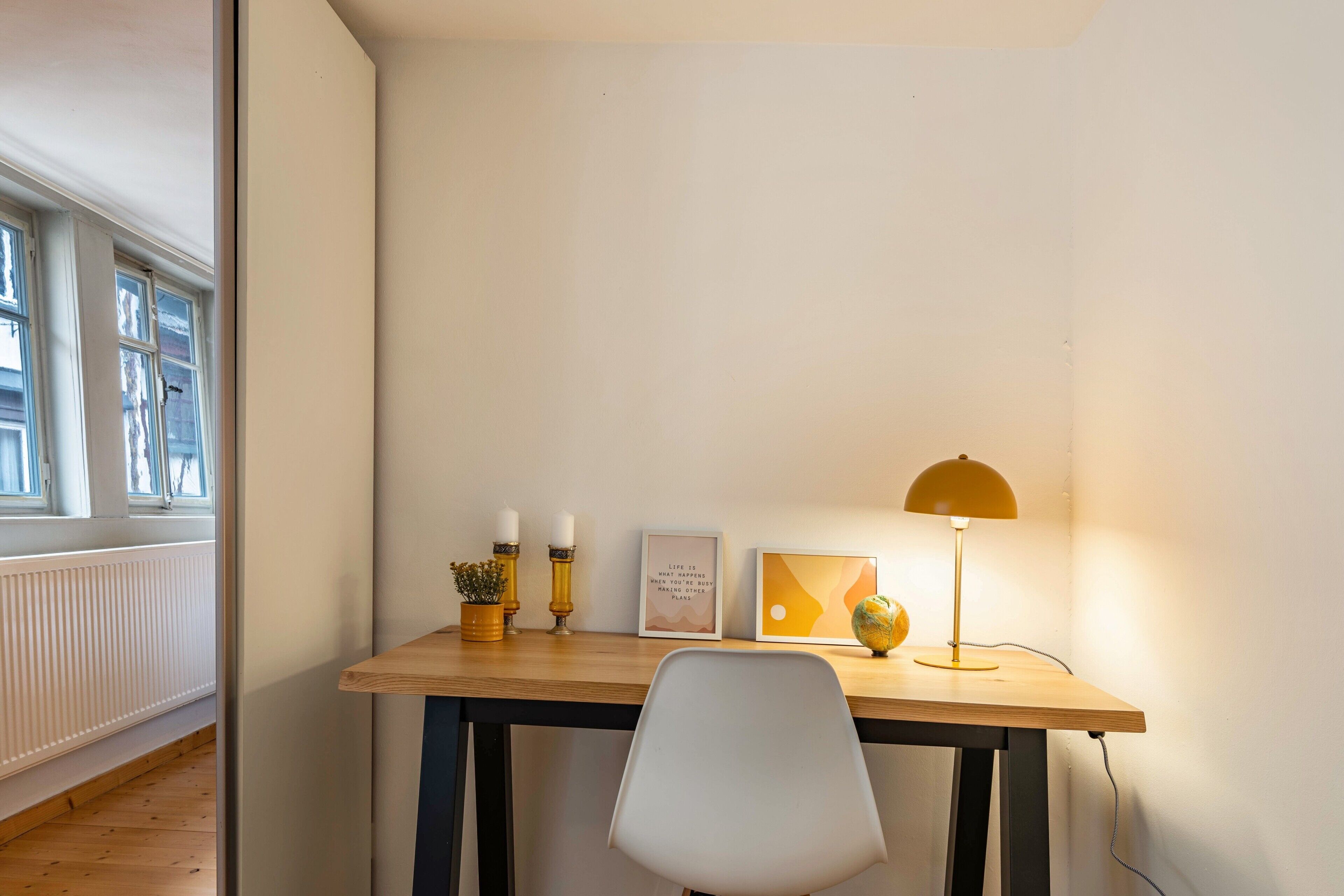 Een kamer met een houten bureau, een witte stoel, een lamp en decoratieve objecten.