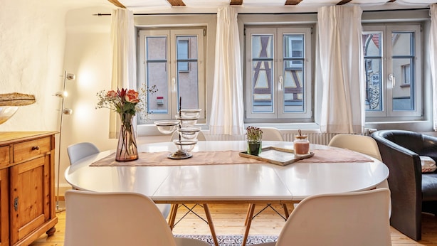Un comedor con una mesa redonda, sillas, un armario de madera y una ventana con cortinas.