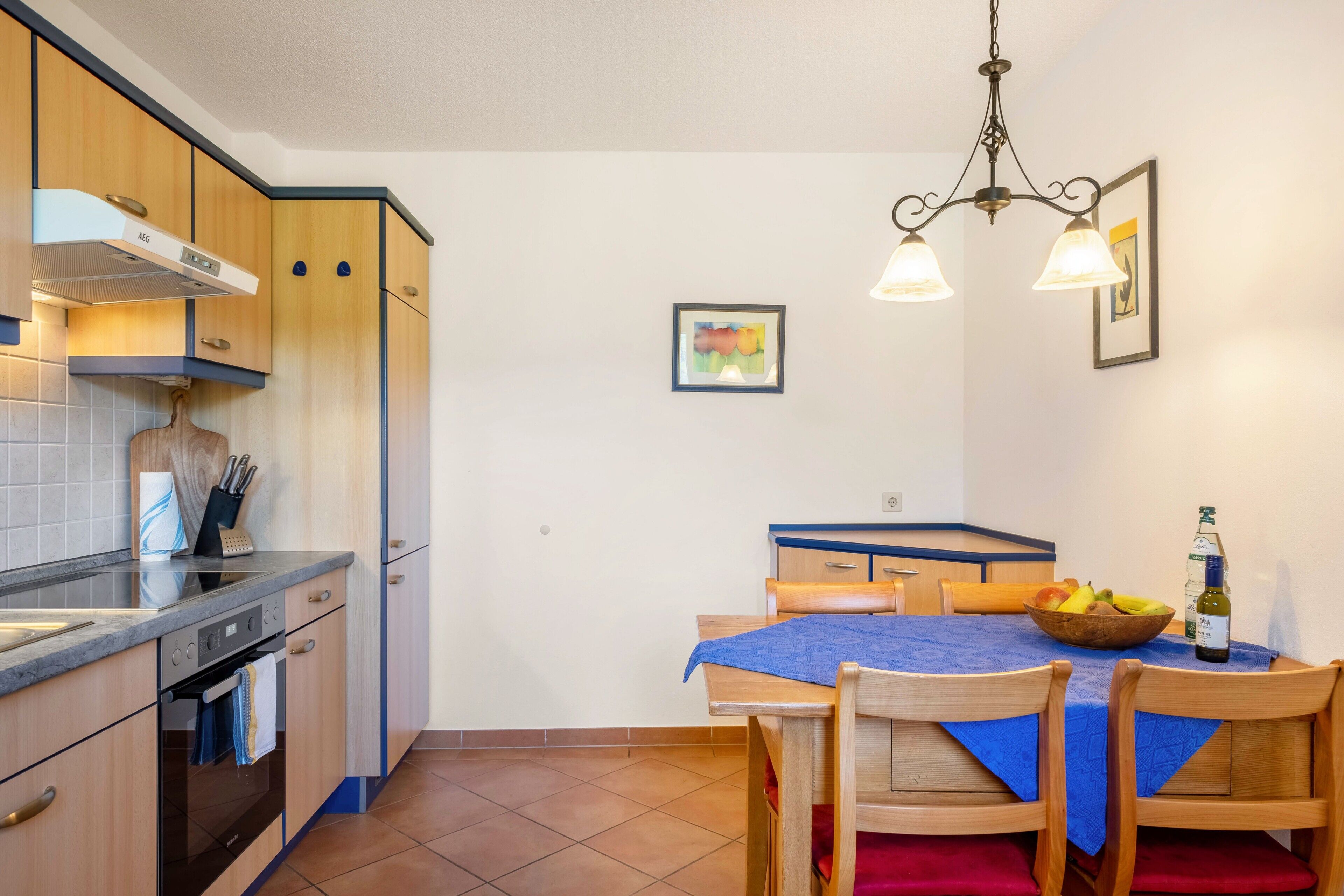 Een keuken met houten kastjes, een fornuis en een eettafel met stoelen.