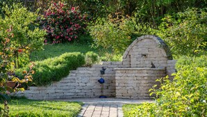Een tuin met een stenen muur, een vogelbeeld en een bakoven.