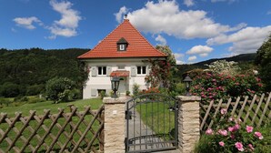 Een huis met twee verdiepingen, een rode pannendak, een stenen poort en een houten hek.