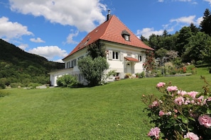 Une maison avec un toit rouge, entourée d’une pelouse bien entretenue et de plantes en fleurs.