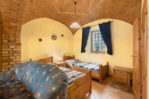 A room with two wooden beds, a brick wall, a wooden ceiling, and a window with curtains.