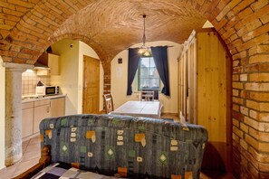 A cozy room with a brick ceiling, a dining table with chairs, a sofa, and a kitchen area with a microwave.