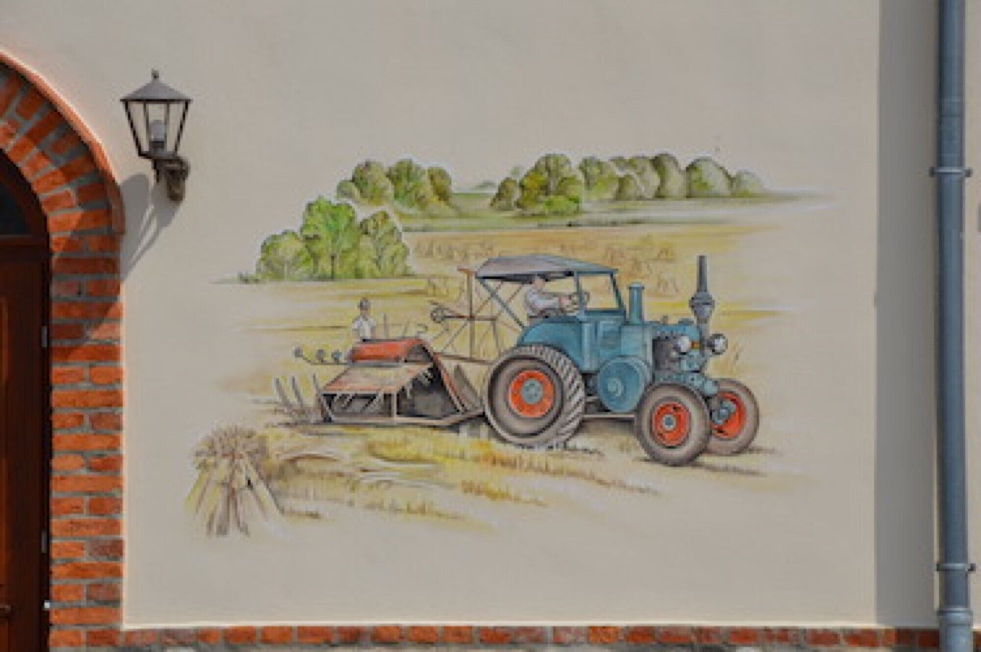 Un mural que muestra un tractor azul con un arado, una persona y un paisaje rural con árboles y un campo.