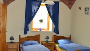 Una habitación con dos camas de madera, una ventana con cortinas azules, una lámpara colgante y techo de ladrillo.