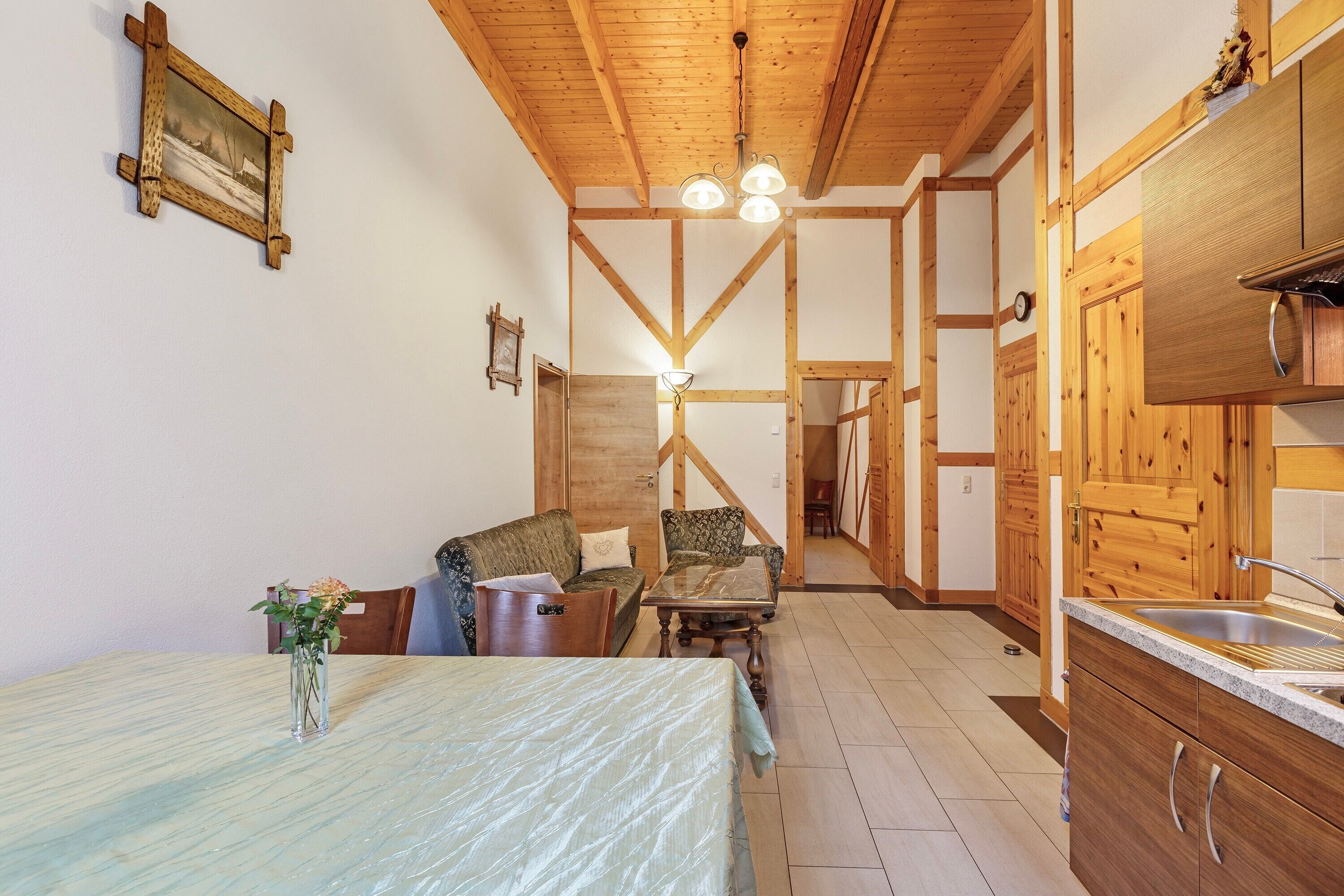 Una habitación con cama, una mesa, una silla, techo de madera y una zona de cocina.