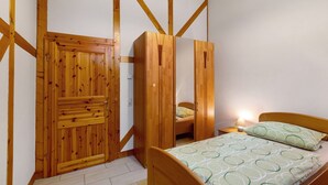 A bedroom with a wooden wardrobe, a bed with patterned bedding, and a nightstand with a lamp.