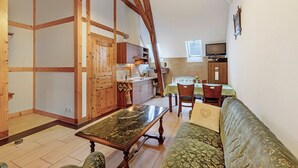 A wooden-framed room with a dining table, a sofa, and a kitchen area with a TV.